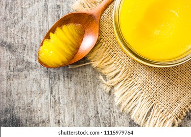 Ghee or clarified butter in jar and wooden spoon on wooden table. Top view. Copyspace