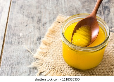 Ghee or clarified butter in jar and wooden spoon on wooden table.