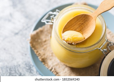 Ghee or clarified butter in jar and wooden spoon on gray table. Top view. Copyspace. Ghee butter have healthy fat and is a common cooking ingredient in many of the Indian food