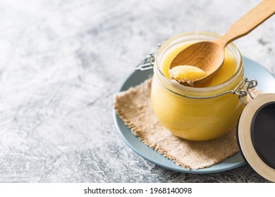 Ghee or clarified butter in jar and wooden spoon on gray table. Top view. Copyspace. Ghee butter have healthy fat and is a common cooking ingredient in many of the Indian food