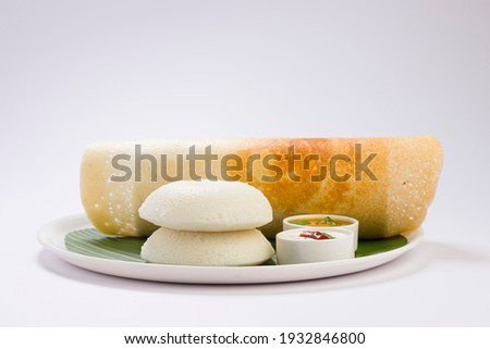 Ghee roast  Dosa and Idlii, south indian main breakfast item which is beautifully arranged in a white plate lined with banana leaf  and curry as sambar and chutney on white background.