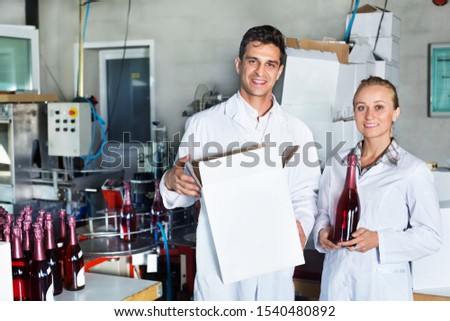Gheerful man and woman winery workers holding carton package with wine bottles on a winery factory. Focus on both persons 