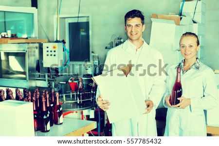 Gheerful man and woman winery workers holding carton package with wine bottles on the winery factory. Focus on both persons