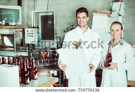 Gheerful man and woman winery workers holding carton package with wine bottles on the winery factory. Focus on both persons