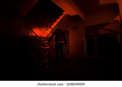 Ghost In Haunted House At Stairs, Mysterious Silhouette Of Ghost Man With Light At Stairs, Horror Scene Of Scary Ghost Spooky Llights . Scary Hall. Halloween Background.