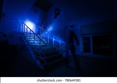 Ghost In Haunted House At Stairs, Mysterious Silhouette Of Ghost Man With Light At Stairs, Horror Scene Of Scary Ghost Spooky Llights . Scary Hall. Halloween Background.