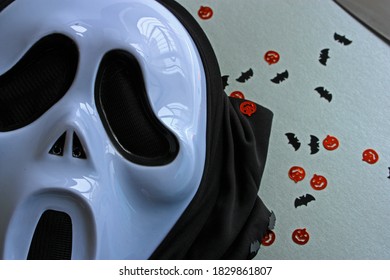 Ghostface Halloween mask. Pumpkin and bats glitter confetti. Grey background.