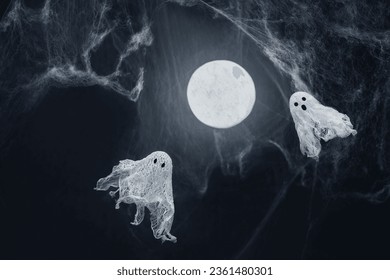 Ghosts of gauze on a dark background with glowing moon and spider web. Creative DIY Halloween decor. Halloween greeting card. Copy space.