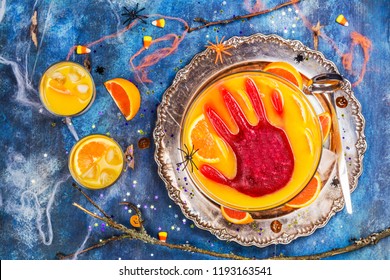 Ghoul's Orange Punch With Bloody Ice Hand In A Glass Bowl On Dark Halloween Background