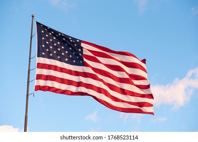 Giant American Flag Flying High Against A Light Blue Sky With A Couple Of Small Clouds With Room For Text.