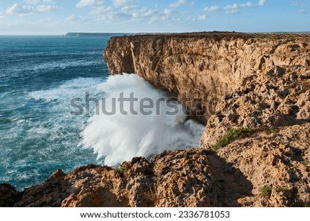 Giant breaking wave in the Atlantic Ocean. Beautiful cliffs near the Sagres Fortress and Cape St. Vincent in the background.