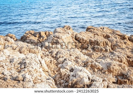 Giant brown rock textured cliff edge isolated on sea waves background on sunny day sunlight.
