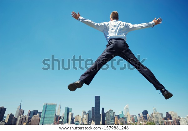 Giant businessman\
doing a spreadeagle jump outdoors in a blue sky celebration above\
the city skyline