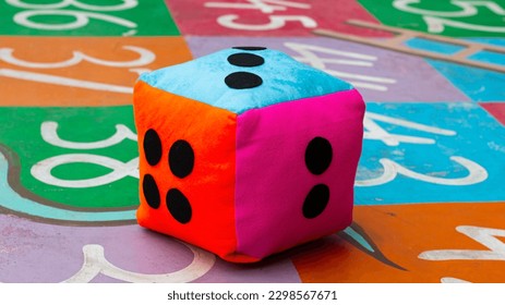 a giant colorful dice showing the number three above during a game of snakes and ladders on the playground - Powered by Shutterstock