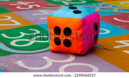 a giant colorful dice showing the number three above during a game of snakes and ladders on the playground