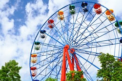 Гигантское колесо обозрения против голубого неба и белого облака, что означает прогулку по парку или ярмарке, состоящую из гигантского вертикального вращающегося колеса с пассажирскими автомобилями, подвешенными на его внешнем краю