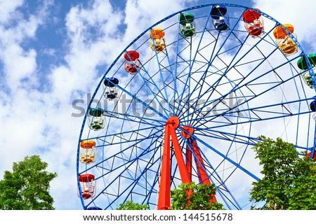 Giant ferris wheel against blue sky and white cloud which mean an amusement-park or fairground ride consisting of a giant vertical revolving wheel with passenger cars suspended on its outer edge