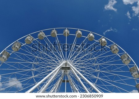 giant ferris wheel detail. white gondolas. steel frame construction. giant spokes in large wheel. leisure and relaxation concept. parks and outdoors. blue sky and white clouds. entertainment and fun.