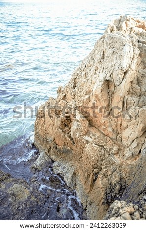 Giant rock textured cliff corner isolated in the blue sea waters on sunny day light