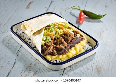 A Giant Tex Mex Burrito Dish, Stuffed With Guacamole, Refried Beans, Shredded Beef And Salad, On A Flat Bread. On A Blue Wooden Table.