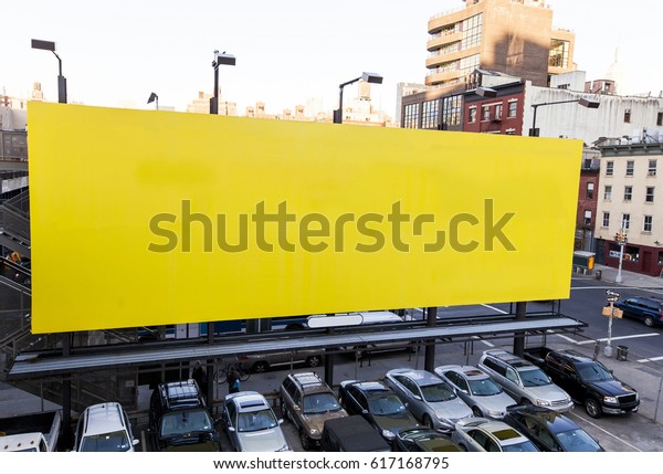 Giant yellow billboard rising above\
the parking lot it is advertising in Manhattan,\
New-York.