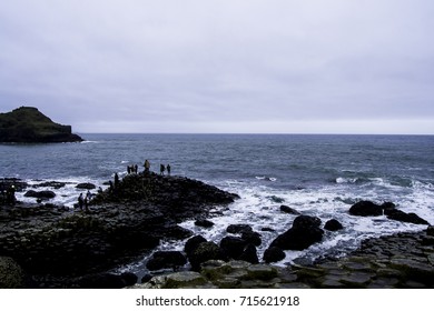 GIANT'S CAUSEWAY, NORTHERN IRELAND - FEBRUARY 2017 - People Walking On Giant's Causeway's Basalt Columns Surrounded By A Wavy Ocean.