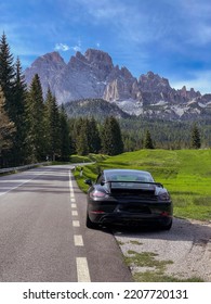 GIAU PASS, DOLOMITES, ITALY, MAY 2022: Sports Car At Roadside Of Winding Road With Gorgeous Mountains In The Background. Idyllic Alps In Spring With Spruce Trees And Mountain Peaks With Spring Snow.