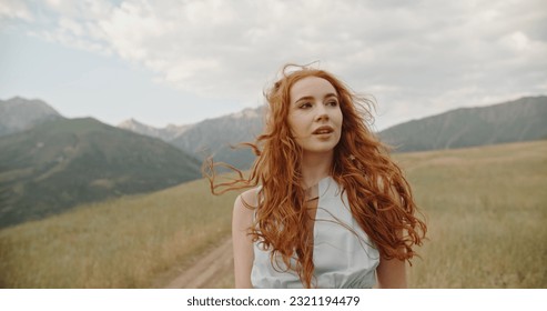 Giel with red hair walking down the wheel trails on meadow with scenic mountain background, looking at camera and smiling - freedom, tranquility concept  - Powered by Shutterstock