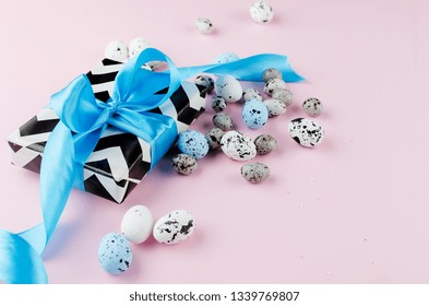 gift with blue ribbon small easter candy eggs and willow twigs on light pink background, top view, copy space, easter greetin card, holiday concept