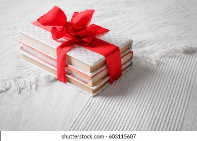 Gift books beautifully wrapped and bandaged with a red ribbon bow on a white coverlet
