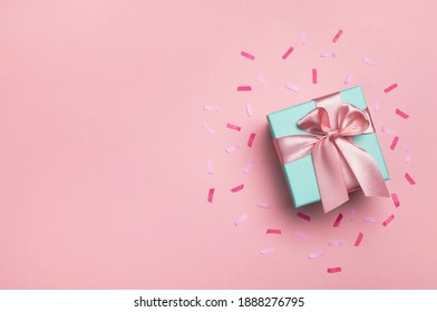 Geschenkbox und Konfetti auf pastellrosa Hintergrund. Geburtstagsfeier, Valentinstag oder Muttertagskarte. Draufsicht, flache Lage, Kopienraum