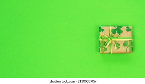 Gift Box In Craft Wrapping Paper With The Image Of Clover Or Shamrock Leaves On A Green Background With Copy Space. St. Patrick's Day Sale Promotion Banner. Gift For St. Patrick's Day Banner. 