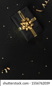 Gift Box With Decorations Gold Confetti On Black Background For Christmas And New Year Concept. Copy Space