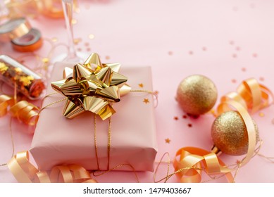 Gift Box With Golden Bow On Pink Coral Background With Stars And Sparkles. Festive Concept Copyspace Top Horizontal View. Sticky Tape, Christmas Balls, Golden Ribbon