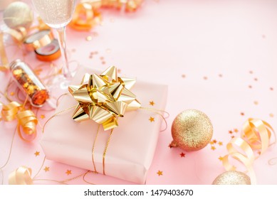 Gift Box With Golden Bow On Pink Coral Background With Stars And Sparkles. Festive Concept Copyspace Top Horizontal View. Sticky Tape, Christmas Balls, Golden Ribbon