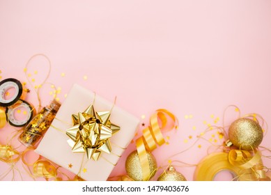 Gift Box With Golden Bow On Pink Coral Background With Stars And Sparkles. Festive Concept Copyspace Top Horizontal View. Sticky Tape, Christmas Balls, Golden Ribbon