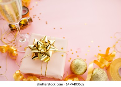 Gift Box With Golden Bow On Pink Coral Background With Stars And Sparkles. Festive Concept Copyspace Top Horizontal View. Sticky Tape, Christmas Balls, Golden Ribbon