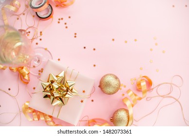 Gift Box With Golden Bow On Pink Coral Background With Stars And Sparkles. Festive Concept Copyspace Top Horizontal View. Sticky Tape, Christmas Balls, Golden Ribbon