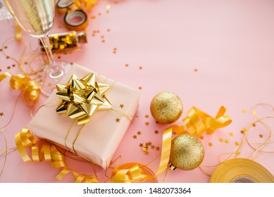 Gift Box With Golden Bow On Pink Coral Background With Stars And Sparkles. Festive Concept Copyspace Top Horizontal View. Sticky Tape, Christmas Balls, Golden Ribbon