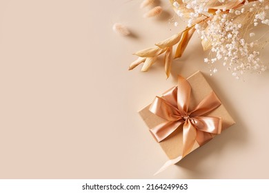 Gift box with golden ribbon and dry grass and flowers on beige background flat lay, top view, copy space - Powered by Shutterstock