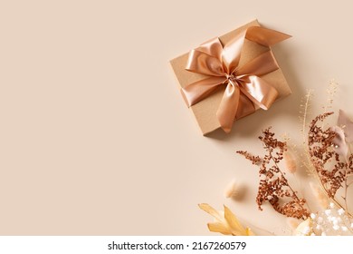 Gift box with golden ribbon and dry grass and flowers on beige background flat lay, top view, copy space - Shutterstock ID 2167260579