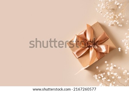 Gift box with golden ribbon and dry grass and flowers on beige background flat lay, top view, copy space