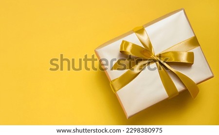 Gift box with golden satin ribbon and bow on yellow background.Holiday gift with Birthday or Christmas present, flat lay, top view, happy mother day copy space