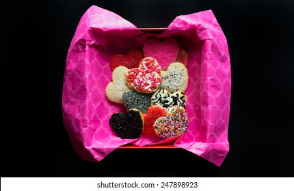 Gift Box Lined With Pink Tissue Paper With Various Valentine's Day Cookies.  Black Background. 