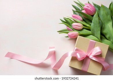 Geschenkbox mit langer rosafarbener Schleife und Tulpen auf hellem Hintergrund