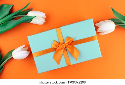 Gift box with an orange bow with white tulips on an orange background. Gift for Women's Day, March 8, Mother's Day or Birthday