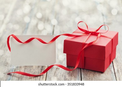 Gift box with red bow ribbon and empty paper note on wooden table for Valentines day - Powered by Shutterstock