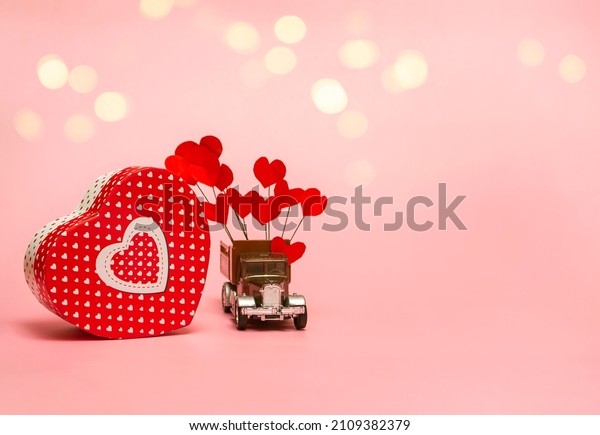 Gift box and retro\
car with paper hearts on a pink background. Valentine\'s day\
concept, anniversary, mother\'s day and happy birthday greeting,\
copyspace, close up