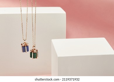 Gift box shape pendant gold necklace on white and pink background. Romantic jewelry. Advertising still life product concept for Valentines Day