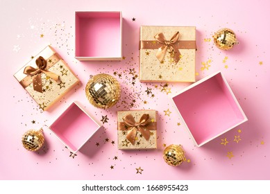 Gift box, shiny gold disco balls, sparkling gold glitter on pink background. New year baubles, star sparkles. New year, Christmas, Valentine's day concept of greetings. Copy text. Top view, flat lay.